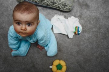baby in blue pajamas looking up at the camera from the floor