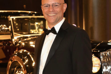 Peter in a tuxedo standing in front of a gleaming classic automobile