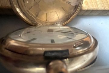 An old-fashioned brass stopwatch sits open on a tabletop