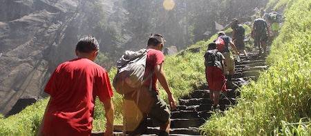 Boy scouts following the leader up a stone stairway next to a waterfall.