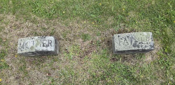Two small headstones viewed from above. One says MOTHER and the other says FATHER.