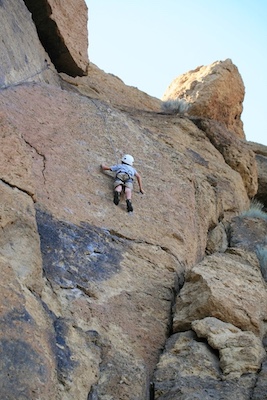 A young rock climber clings to a cliff wall, halfway up. To achieve results, he needs to focus on grabbing the next hold, not on being at the top.