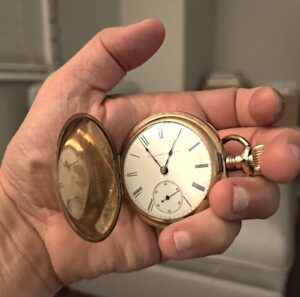 A hand holds an old style pocket watch