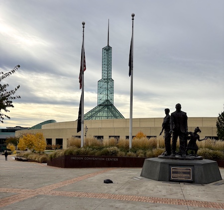 Photo of the Portland Convention Center with a statue in the front and flags lying against the poles on a windless day.