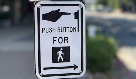 A "push button for crosswalk sign" sign on a post with a blurred background.