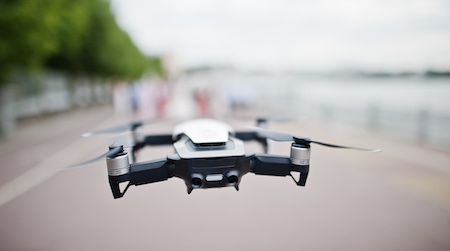 A drone with four propellers flies level and stable along a populated walkway, with all the background blurred.