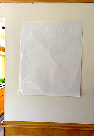 A blank piece of flipchart paper on a beige wall, indicating visual white space
