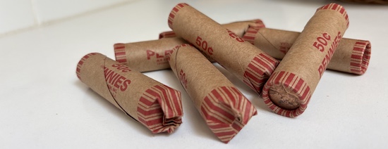 A pile of rolls of pennies, each roll worth 50 cents, on a white countertop.