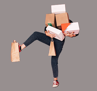 A person holding too many packages, including one dangling from her raised foot.