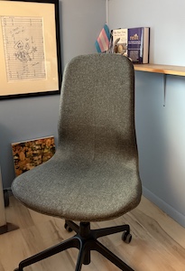 An empty desk chair with a bookshelf and art on the wall behind.  It's filled with uncertainty.